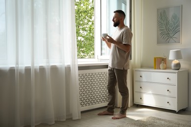 Photo of Harmony. Man with cup of drink near window at home