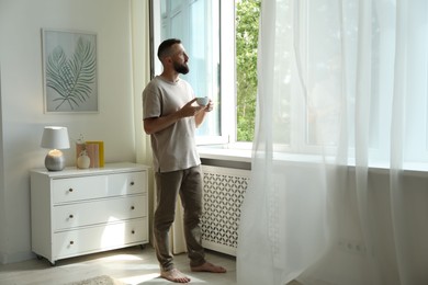 Photo of Harmony. Man with cup of drink near window at home