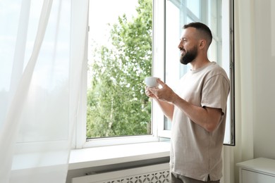 Photo of Harmony. Man with cup of drink near window at home