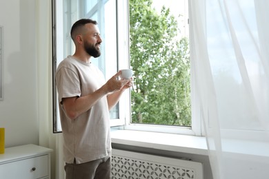 Photo of Harmony. Man with cup of drink near window at home