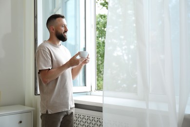 Photo of Harmony. Man with cup of drink near window at home