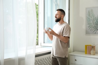 Photo of Harmony. Man with cup of drink near window at home