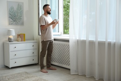 Photo of Harmony. Man with cup of drink near window at home