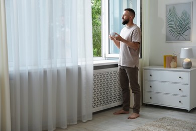 Photo of Harmony. Man with cup of drink near window at home