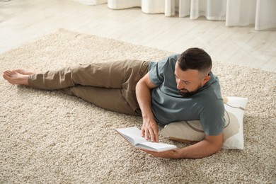 Photo of Harmony. Man reading book on rug at home
