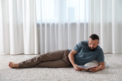 Photo of Harmony. Man reading book on rug at home