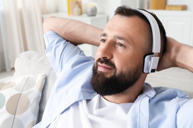 Photo of Harmony. Man listening to music in headphones on sofa at home