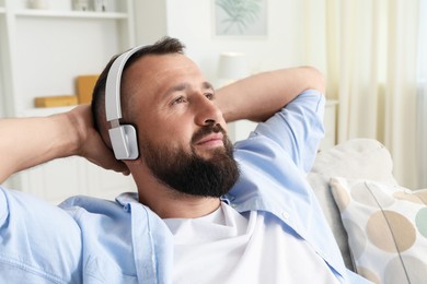 Photo of Harmony. Man listening to music in headphones on sofa at home