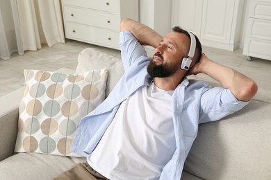 Photo of Harmony. Man listening to music in headphones on sofa at home
