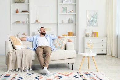 Photo of Harmony. Man listening to music in headphones on sofa at home