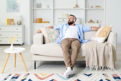 Photo of Harmony. Man listening to music in headphones on sofa at home