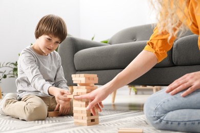 Photo of Mother and her son playing with wooden constructor blocks on floor at home, closeup