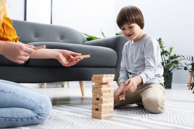 Photo of Mother and her son playing with wooden constructor blocks on floor at home, closeup