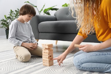 Photo of Mother and her son playing with wooden constructor blocks on floor at home, closeup