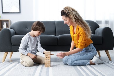 Photo of Mother and her son playing with wooden constructor blocks on floor at home