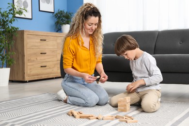 Photo of Mother and her son playing with wooden constructor blocks on floor at home