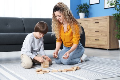 Photo of Mother and her son playing with wooden constructor blocks on floor at home