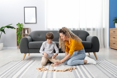 Photo of Mother and her son playing with wooden constructor blocks on floor at home