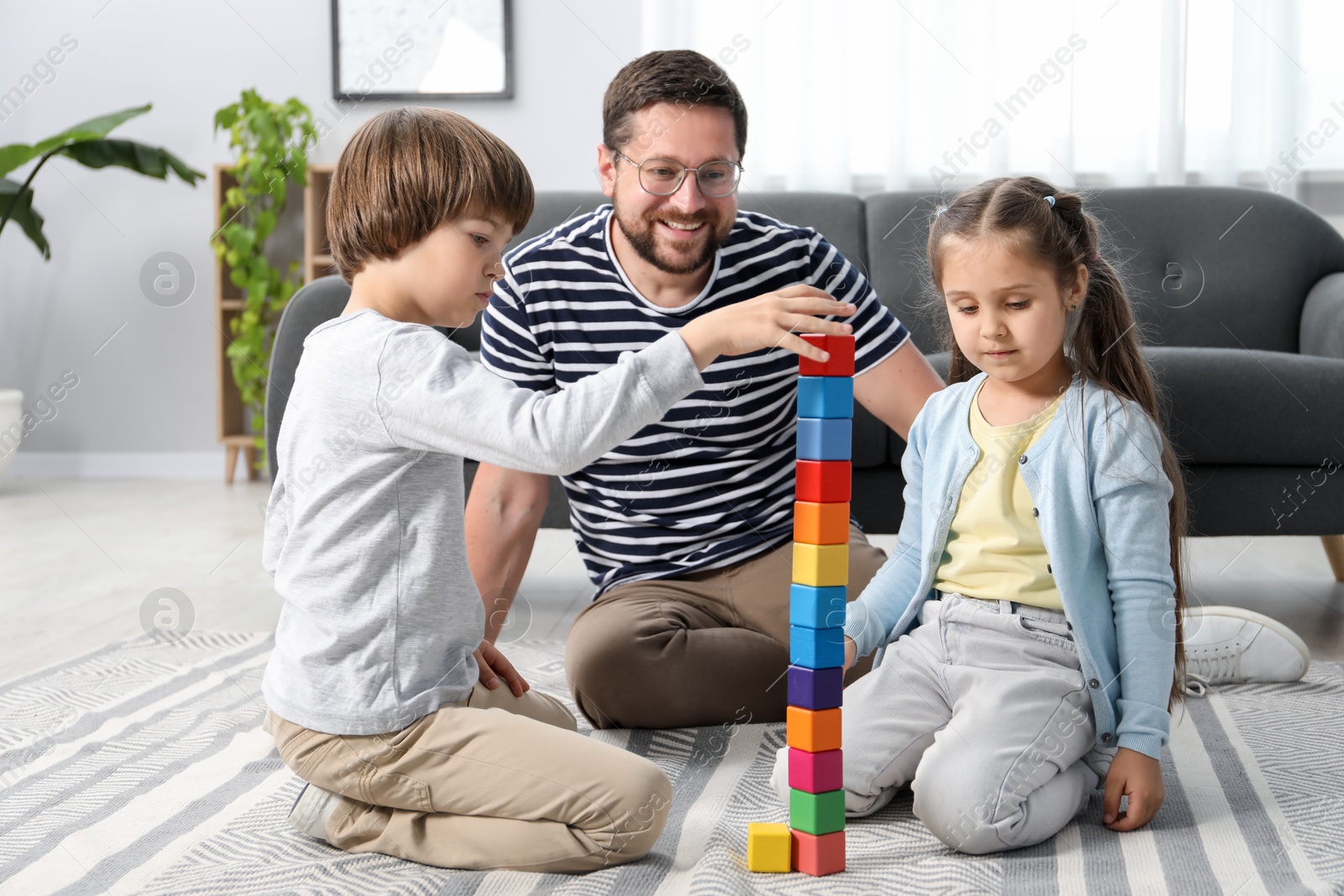 Father and his children playing with colorful cubes on floor at home Photo of Father and his children playing with colorful cubes on floor at home