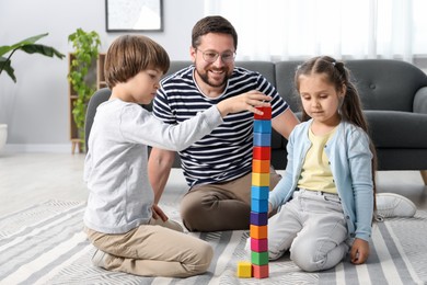Photo of Father and his children playing with colorful cubes on floor at home