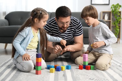 Photo of Father and his children playing with colorful cubes on floor at home