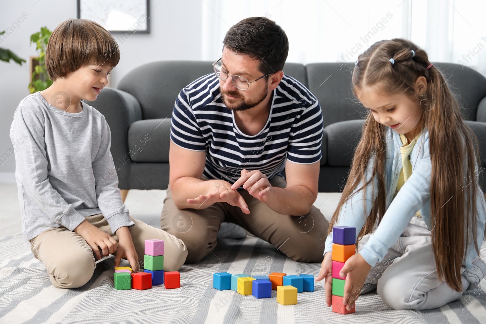 Father and his children playing with colorful cubes on floor at home Photo of Father and his children playing with colorful cubes on floor at home