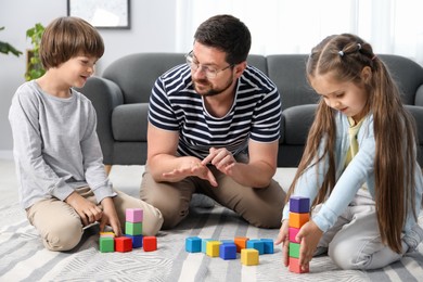 Photo of Father and his children playing with colorful cubes on floor at home