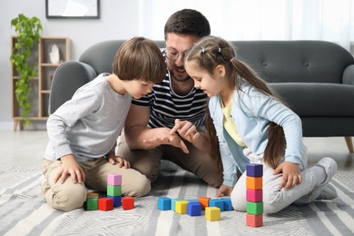 Photo of Father and his children playing with colorful cubes on floor at home