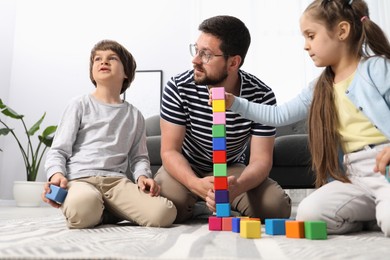 Photo of Father and his children playing with colorful cubes on floor at home, low angle view