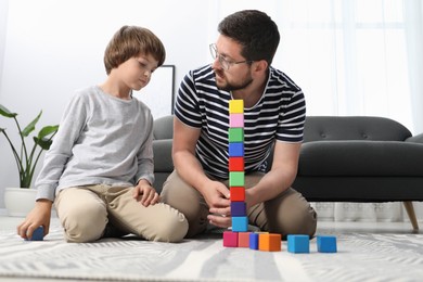 Photo of Father and his son playing with colorful cubes on floor at home, low angle view