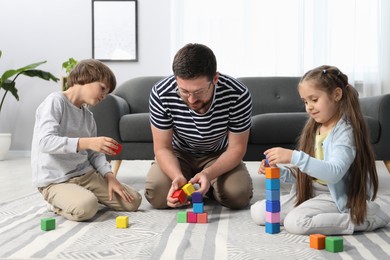 Photo of Father and his children playing with colorful cubes on floor at home