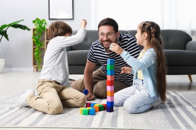 Photo of Father and his children playing with colorful cubes on floor at home