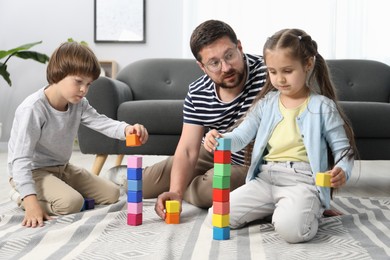 Photo of Father and his children playing with colorful cubes on floor at home