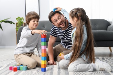 Photo of Father and his children playing with colorful cubes on floor at home