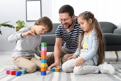 Photo of Father and his children playing with colorful cubes on floor at home