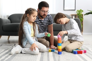 Photo of Father and his children playing with colorful cubes on floor at home