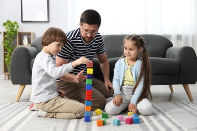 Photo of Father and his children playing with colorful cubes on floor at home