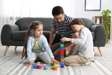 Photo of Father and his children playing with colorful cubes on floor at home
