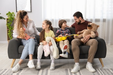 Photo of Children and their parents playing with different toys on sofa at home