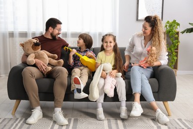 Photo of Children and their parents playing with different toys on sofa at home