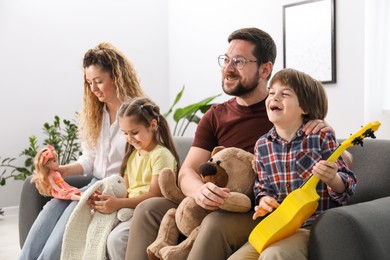 Photo of Children and their parents playing with different toys on sofa at home