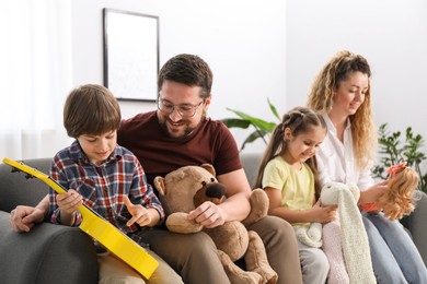Photo of Children and their parents playing with different toys on sofa at home