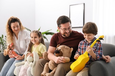 Photo of Children and their parents playing with different toys on sofa at home