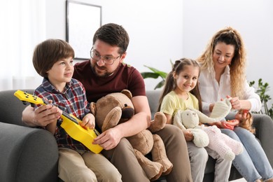 Photo of Children and their parents playing with different toys on sofa at home