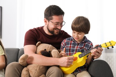Photo of Father and his son playing toy guitar on sofa at home
