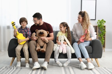 Photo of Children and their parents playing with different toys on sofa at home