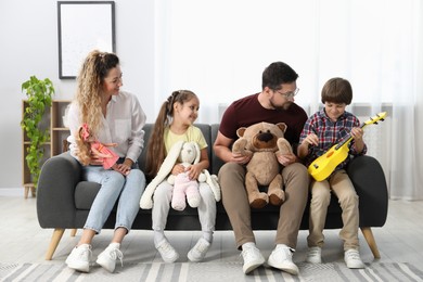 Photo of Children and their parents playing with different toys on sofa at home