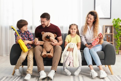 Photo of Children and their parents playing with different toys on sofa at home