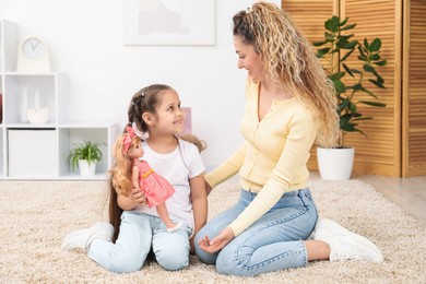 Photo of Mother and her daughter playing with doll on floor at home