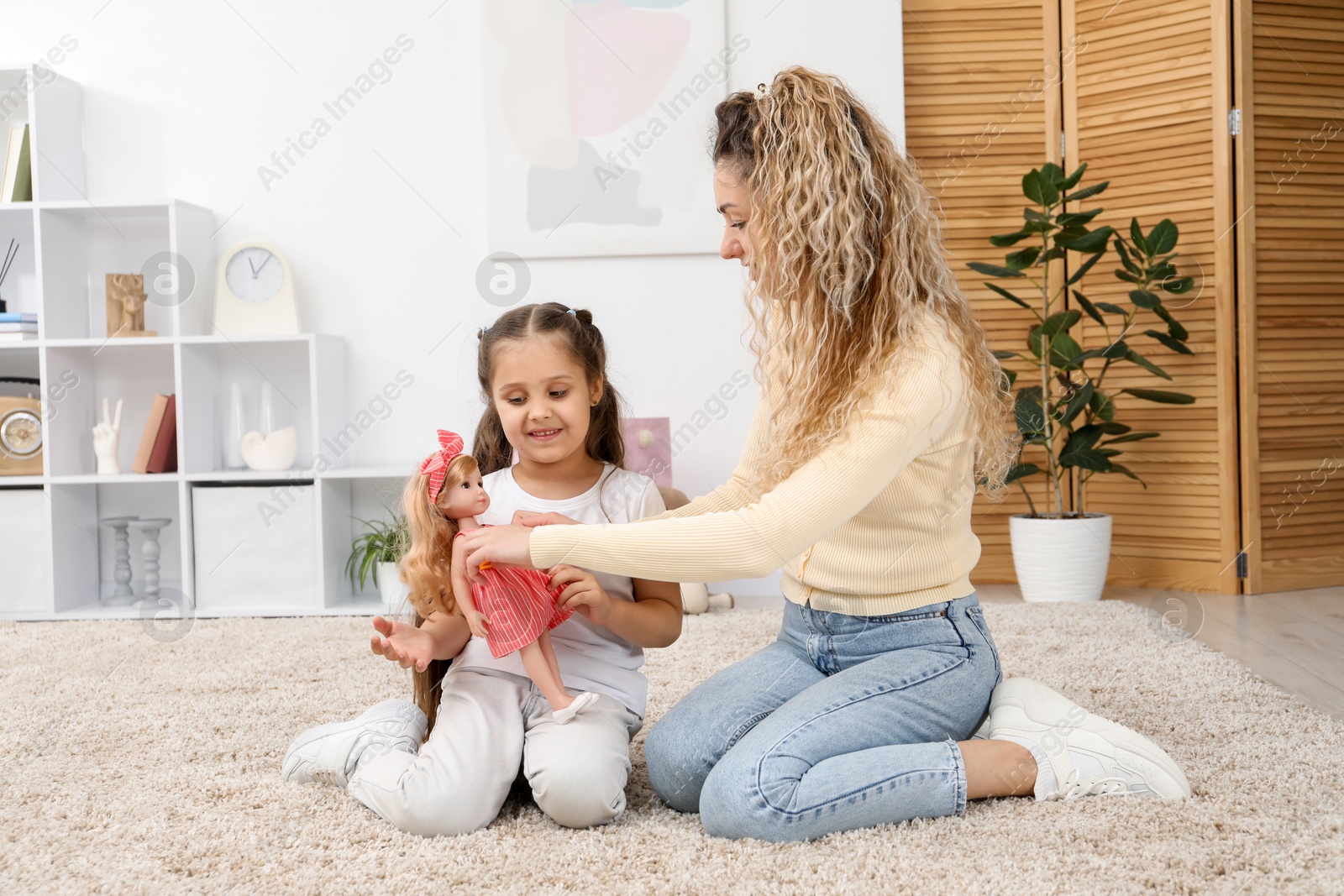 Mother and her daughter playing with doll on floor at home Photo of Mother and her daughter playing with doll on floor at home